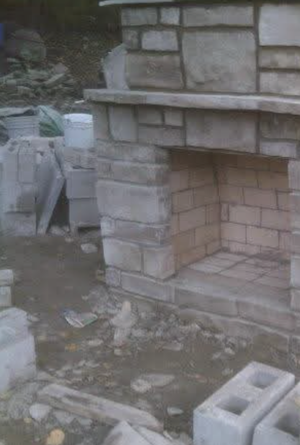 Brickwork in progress around an outdoor masonry fireplace and stone surround
