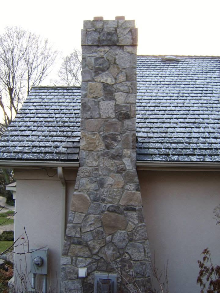 Custom stone chimney built with mixed natural stone on a residential roofline