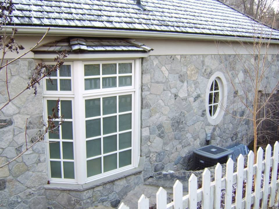 Natural stone exterior wall with white window trim and a round accent window